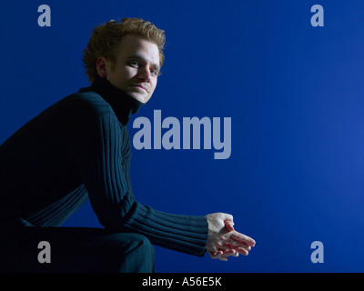 Young man sitting against blue background, portrait Stock Photo