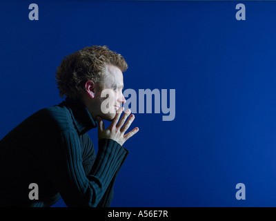 Young man sitting against blue background, portrait Stock Photo