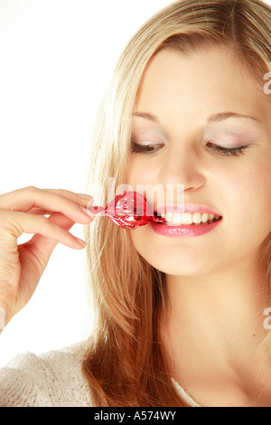 Young woman holding wrapped candy between teeth, close-up Stock Photo
