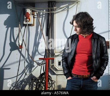 Young man in  black leather jacket standing amongst cables and pipework Stock Photo
