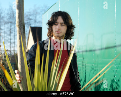 Young man in red and black leather jacket standing amongst a spikey plant Stock Photo