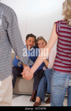 Teenage couple holding hands, parents sitting on sofa Stock Photo