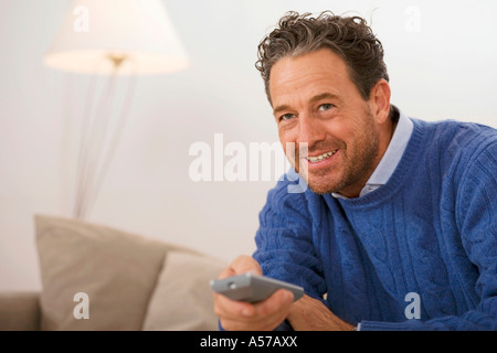 Man sitting on sofa, holding remote control Stock Photo