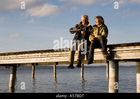 Senior couple sitting on jetty Stock Photo