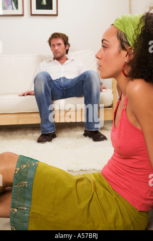 Young woman sitting on floor, young man in background Stock Photo