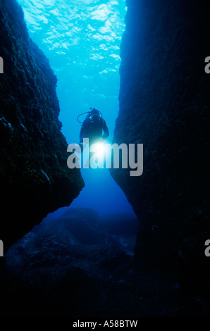 Underwater scuba diver shines a light while swimming through a cave. Stock Photo