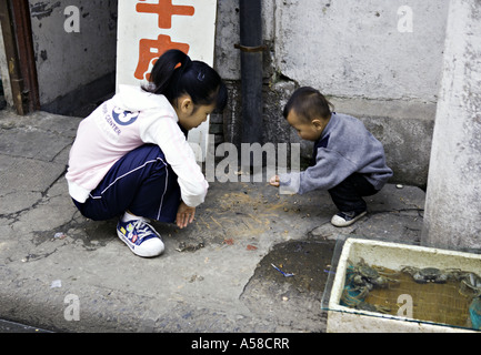 CHINA SHANGHAI Chinese children squat on the sidewalk outside their parent s seafood shop to play a game with chalk Stock Photo