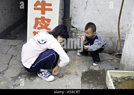 CHINA SHANGHAI Chinese children squat on the sidewalk outside their parent s seafood shop to play a game with chalk Stock Photo