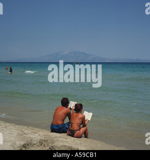 Couple sitting together reading books at water's edge on Alikes Beach east coast Zakynthos Island The Greek Islands Greece Stock Photo