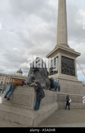 Two young women climbing onto a lion in trafalgar square london uk Stock Photo