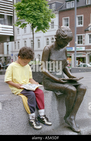 A small boy reading next to a statue of someone reading, in Aachen, Germany. Stock Photo