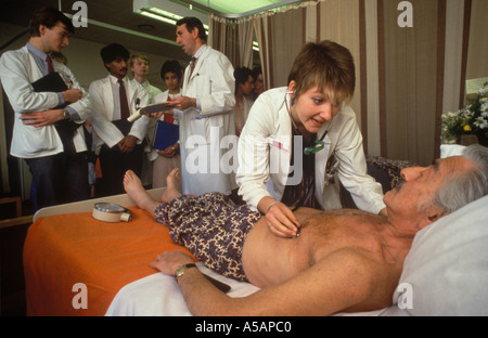 NHS Female junior doctor checking male elderly patient ward round senior doctor in attendance teaching hospital St Georges South London UK 1980s Stock Photo