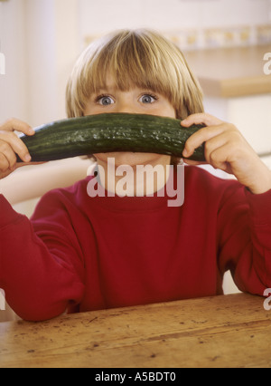 Young boy sitting in a kitchen, with a cucumber - having fun Stock Photo