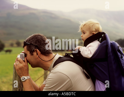 Father on holiday at Buttermere in the Lake District in UK taking photographs with his baby daughter in a backpack Stock Photo