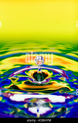 Multicoloured water drop and ripple. Water on a plate mirror with reflected colour background. Stock Photo