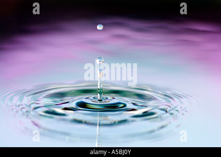 Coloured water drop and ripple. Water on a plate mirror with reflected colour background. Stock Photo
