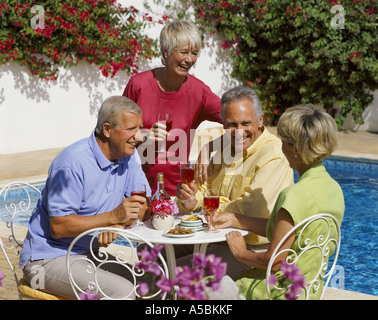 mature couples drinking wine by the poolside in summer sun Stock Photo