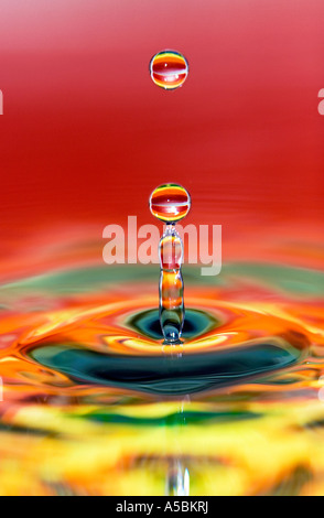 Water drop on orange, red, yellow gradient water mirrored surface. Water on a plate mirror with reflected colour Stock Photo