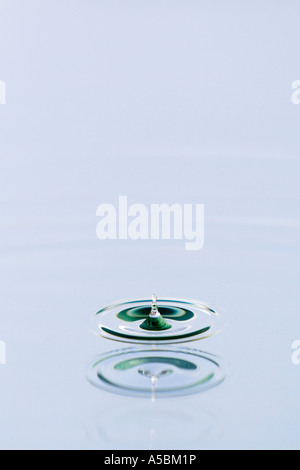 Water drop reflected onto blue coloured mirrored background. Water on a plate mirror with reflected colour Stock Photo