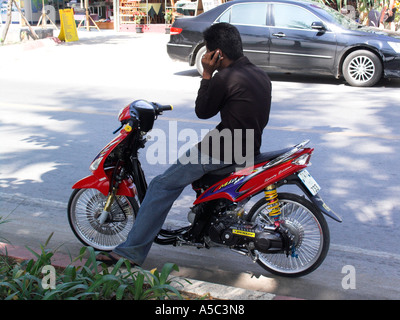 Young man on sporty motorcycle talks on mobile phone Ao Nang beach near Krabi Thailand Stock Photo