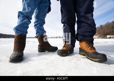 Two boys wearing boots and standing on a frozen lake and seen from the knees down. Stock Photo