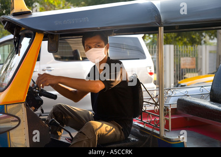 Smog protection in the  busy capital city Bankok.  Driver of Tuk-tuks taxi wearing pollution filter mask filtering  vehicle exhaust fumes. Stock Photo