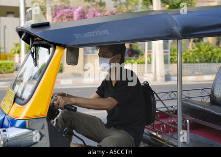 Smog protection in the  busy capital city Bankok.  Driver of Tuk-tuks taxi wearing pollution filter mask filtering  vehicle exhaust fumes. Stock Photo