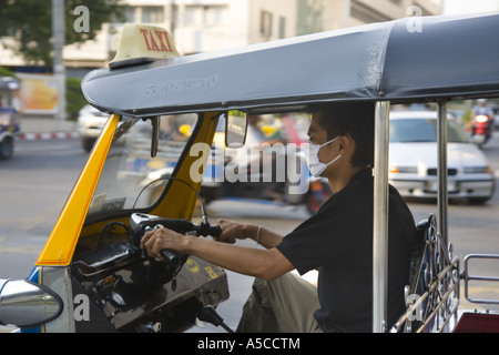 Smog protection in the  busy capital city Bankok.  Driver of Tuk-tuks taxi wearing pollution filter mask filtering  vehicle exhaust fumes. Stock Photo