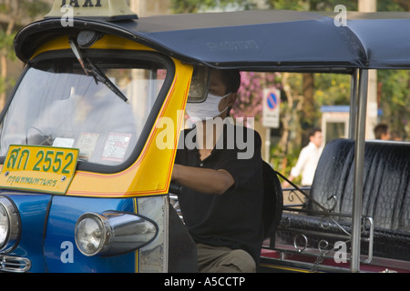 Smog protection in the  busy capital city Bankok.  Driver of Tuk-tuks taxi wearing pollution filter mask filtering  vehicle exhaust fumes. Stock Photo