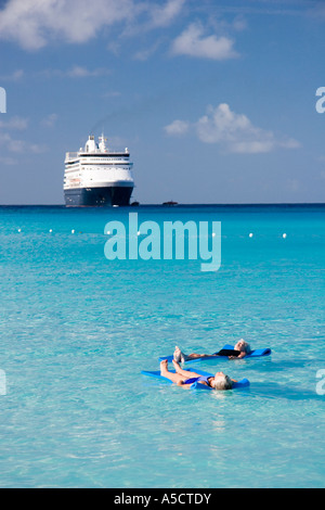 Cruise ship passengers on water matresses at Half Moon Cay Bahamas with Holland America cruise ship ms Veendam in background Stock Photo