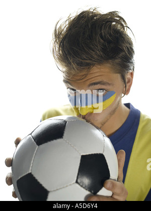 Young man with Ukrainian flag painted on face, kissing soccer ball, portrait Stock Photo