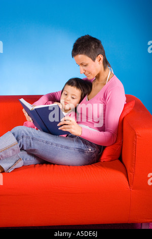 woman and her dauther sitting on the red sofa and reading the book Stock Photo