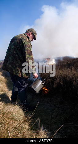 Gamekeeper dousing fire during controlled heather burning on the North Yorkshire Moors, UK Stock Photo