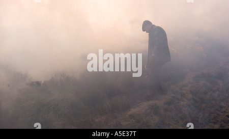 Gamekeeper in smoke tending controlled heather burning on the North Yorkshire Moors, UK Stock Photo