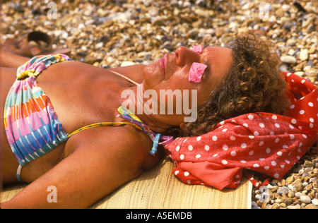 Sleep sleeping British lady sun tanning sun tanned sleeping beach sun  pink lips matching pink paper covering her eyes Brighton Sussex  HOMER SYKES Stock Photo