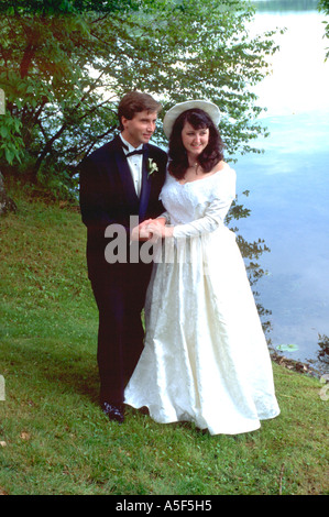 Bride and Groom holding hands by Roy Lake after wedding ceremony age 25. Nisswa Minnesota USA Stock Photo
