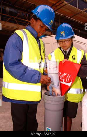 Schoolchildren putting itmes newspaper in time capsule for burial on new housing development, Southwark, London, UK. Stock Photo