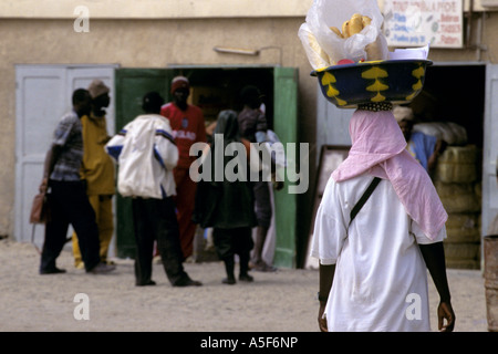 Street scene with woman in traditional clothing carrying bowl of vegetables on head, rear view, Nouakchott,  Mauritania, Africa Stock Photo