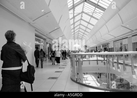 black and white image off a busy shopping centre, lots off people walking about and sitting down resting on the benches Stock Photo