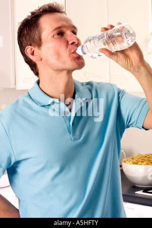 MAN IN KITCHEN DRINKING FROM BOTTLE OF WATER Stock Photo