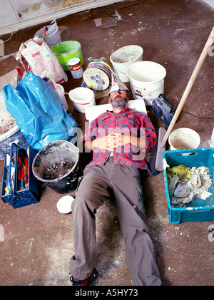 MR PR exhausted handyman do it yourselfer renovating a flat lying in middle of his tools and colour buckets Stock Photo