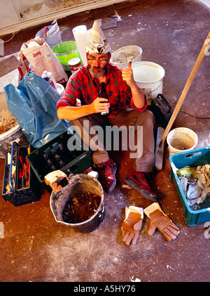 MR PR handyman do it yourselfer renovating a flat having a break and drinking a beer in middle of his tools and colour buckets Stock Photo