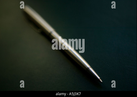 A silver colored metal ballpoint pen stands alone on a dark green surface February 2006 Stock Photo
