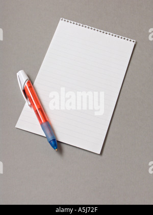 A spiral bound notepad with a red pen on a plain grey background Stock Photo