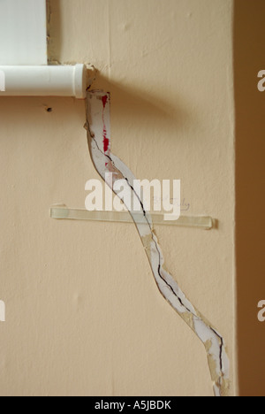 House interior damage on wall with glass strip glued across crack by insurance company to monitor further movement Stock Photo