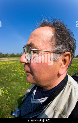 Man with camera standing in grass field with blue sky and cowslips in the background Stock Photo