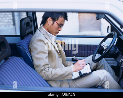 Asian Man making notes in a car Stock Photo