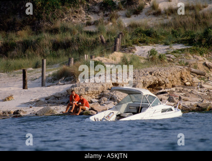 VA Chesapeake Beach Boat sinking near shore with its passengers resting safely on rocks Stock Photo