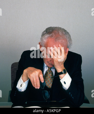 Elderly businessman wearing a suit in his office overworked and tired sitting at his desk. White collar job USA Stock Photo