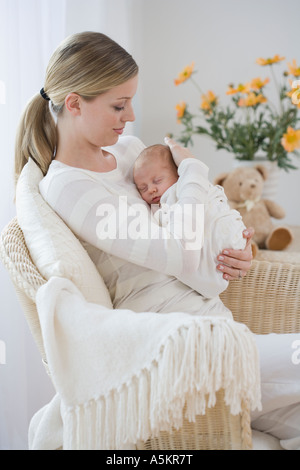 Mother rocking newborn baby in chair Stock Photo